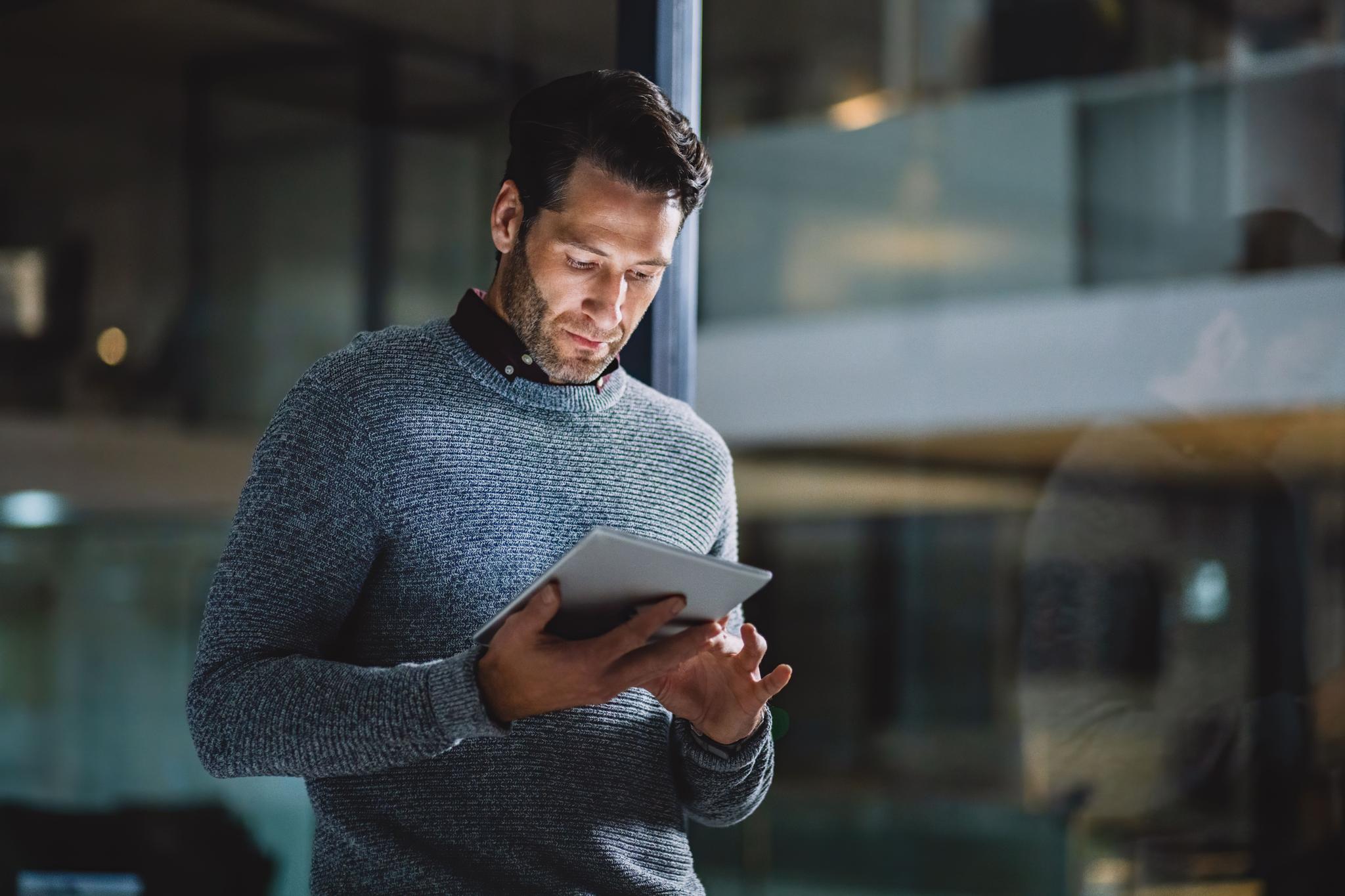 A businessman standing alone in his office and using a tablet